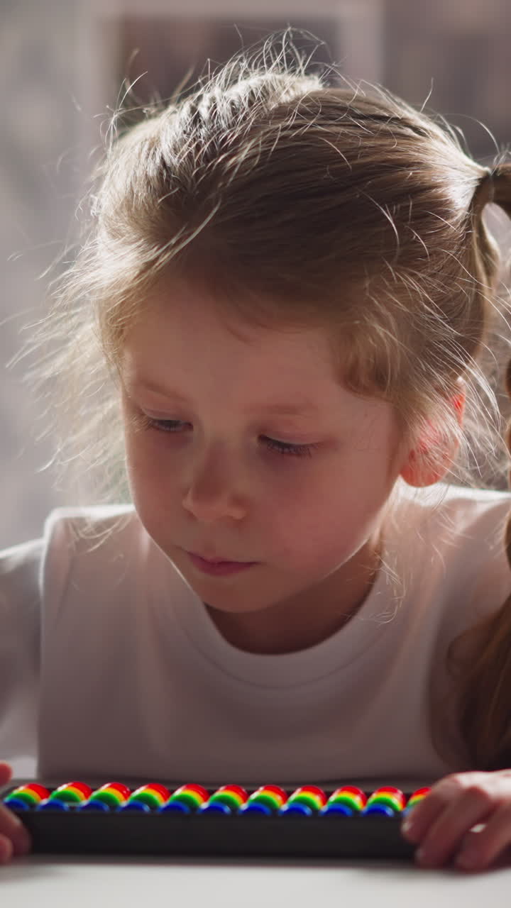 Tranquil little girl in white sweatshirt with colorful abacus solves tasks sitting at workplace during mathematics lesson close view slow motion