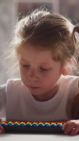 tranquil little girl in white sweatshirt with colorful abacus solves tasks sitting at workplace during mathematics lesson close view slow motion
