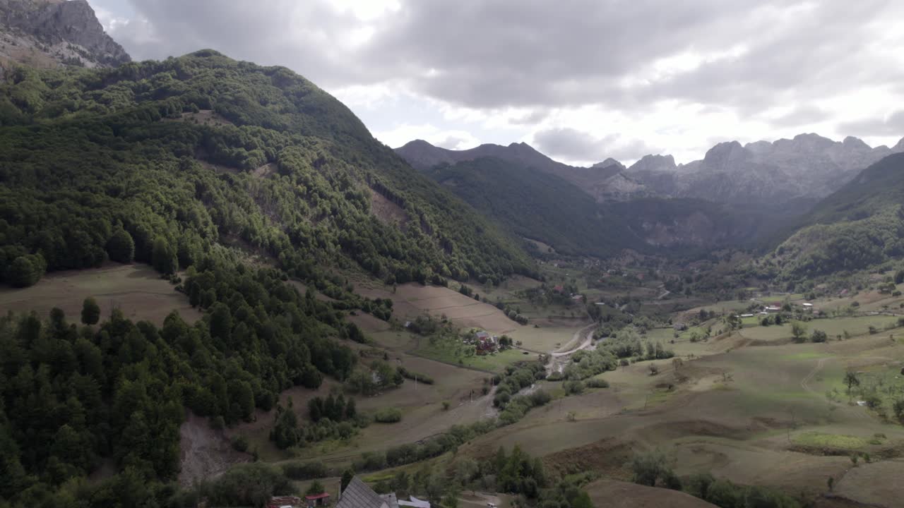 video drone del avion frontal avanzando sobre el valle de lepushë sobre el rio lëpusha, el sh20 en albania, se pueden ver casitas del pueblo, un cielo algo nublado y el rio seco