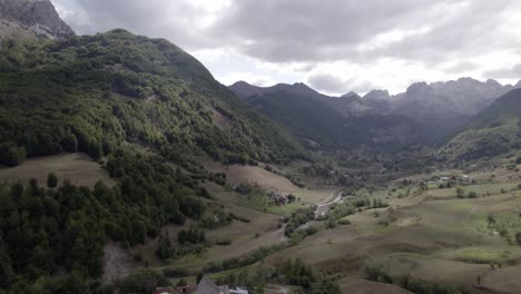 Drone-video-of-the-frontal-plane-advancing-over-the-Lepushë-valley-above-the-Lëpusha-river,-the-sh20-in-Albania,-you-can-see-small-houses-of-the-town,-a-somewhat-cloudy-sky-and-the-dry-river