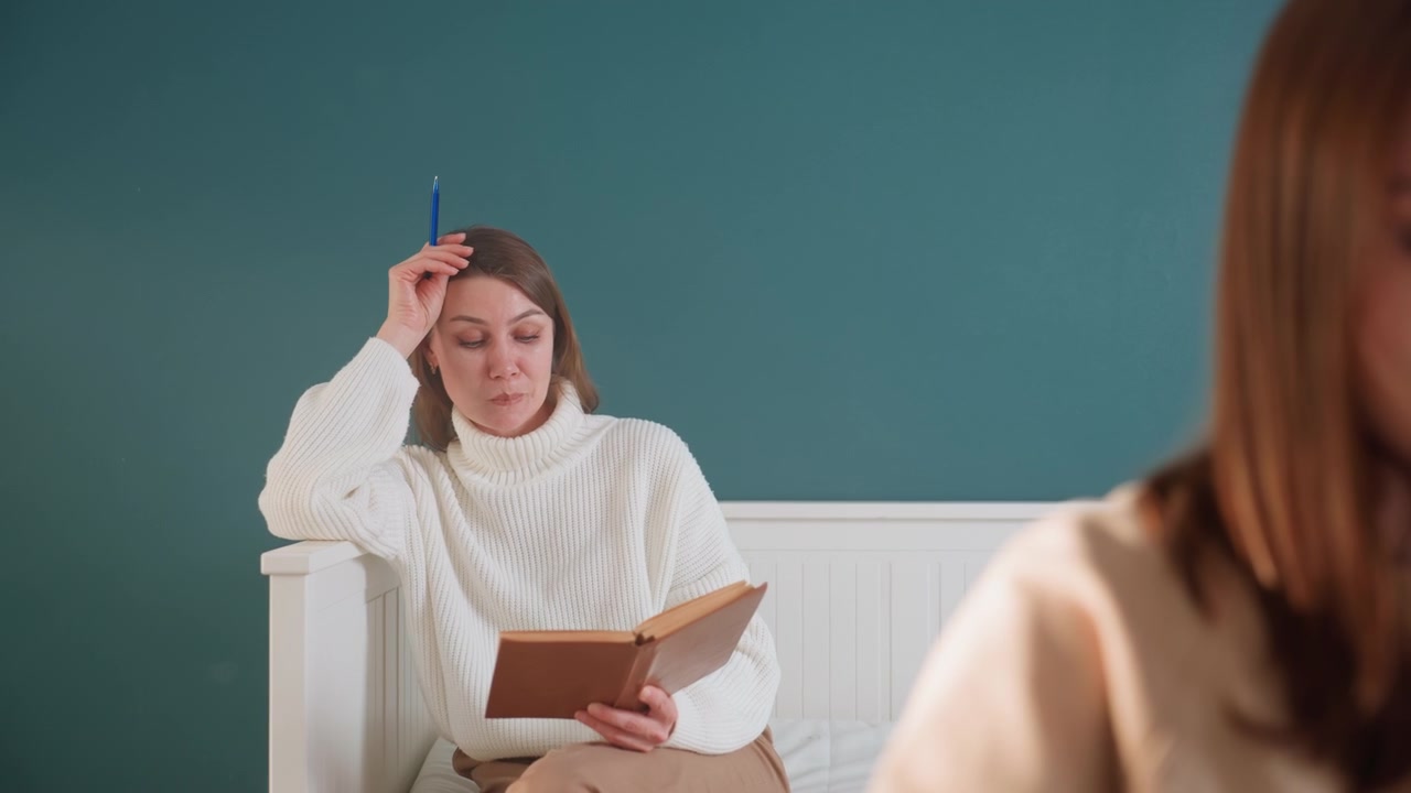 Due donne in una accogliente sala studio, sessione di tutoraggio con l'alunna sullo sfondo che alza la penna mentre la studentessa in primo piano si concentra sul quaderno di esercizi e sugli esercizi di grammatica, tranquilla parete verde acqua, coaching di supporto e appunti di correzione