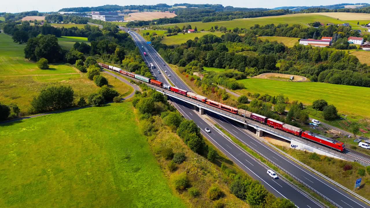 Long Freight Train with Red Locomotive Passing Over Highway Bridge in Scenic Countryside