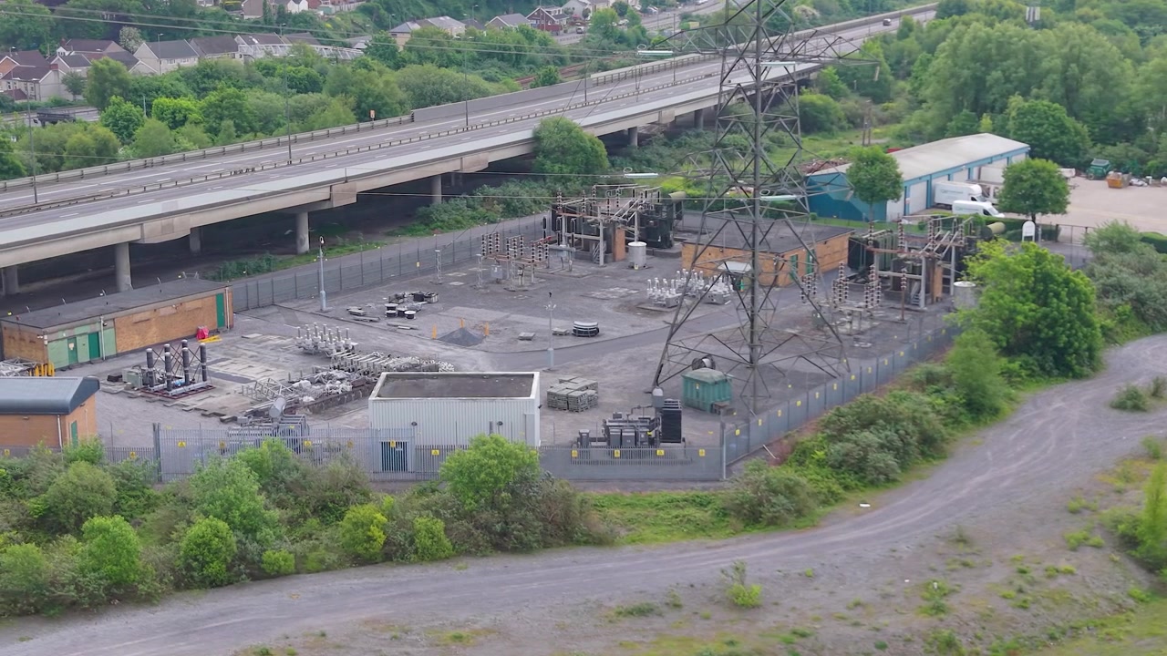 Circulerende luchtopname van een hoogspanningsonderstation nabij een snelwegviaduct. Kritieke infrastructuur van een modern elektriciteitsnet, energiedistributie, industriële engineering. 4K