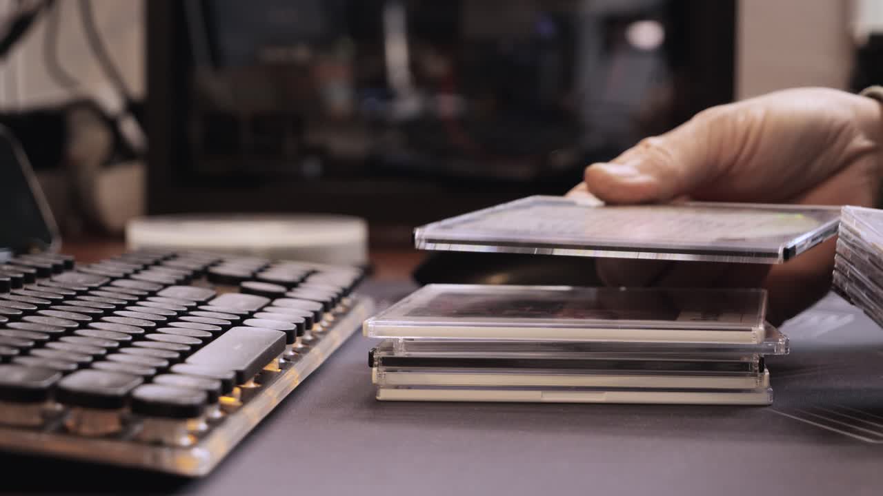 Close up of hands stacking CD cases near retro keyboard on desk in home office or media archive.