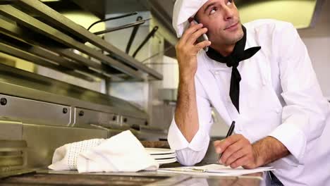 handsome chef writing on clipboard while talking on phone