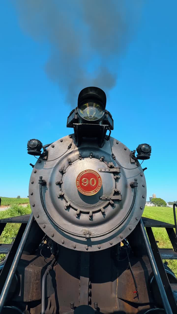 Boston, USA, 8 maggio 2025: Primo piano frontale di una locomotiva a vapore. Inquadratura frontale dal basso di una locomotiva a vapore argentata numero 90 che emette fumo contro un cielo azzurro limpido e campi verdi.