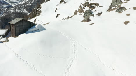 aerial of footsteps in snow towards wooden cabins in mountains