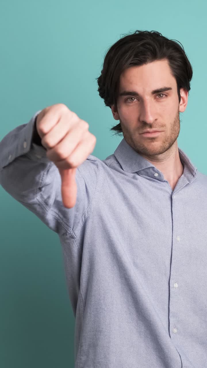 Upset man showing thumb down in blue studio