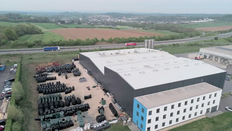 aerial backward, over an industrial building along the highway with some trucks passing, big yard full of plastic merchandises