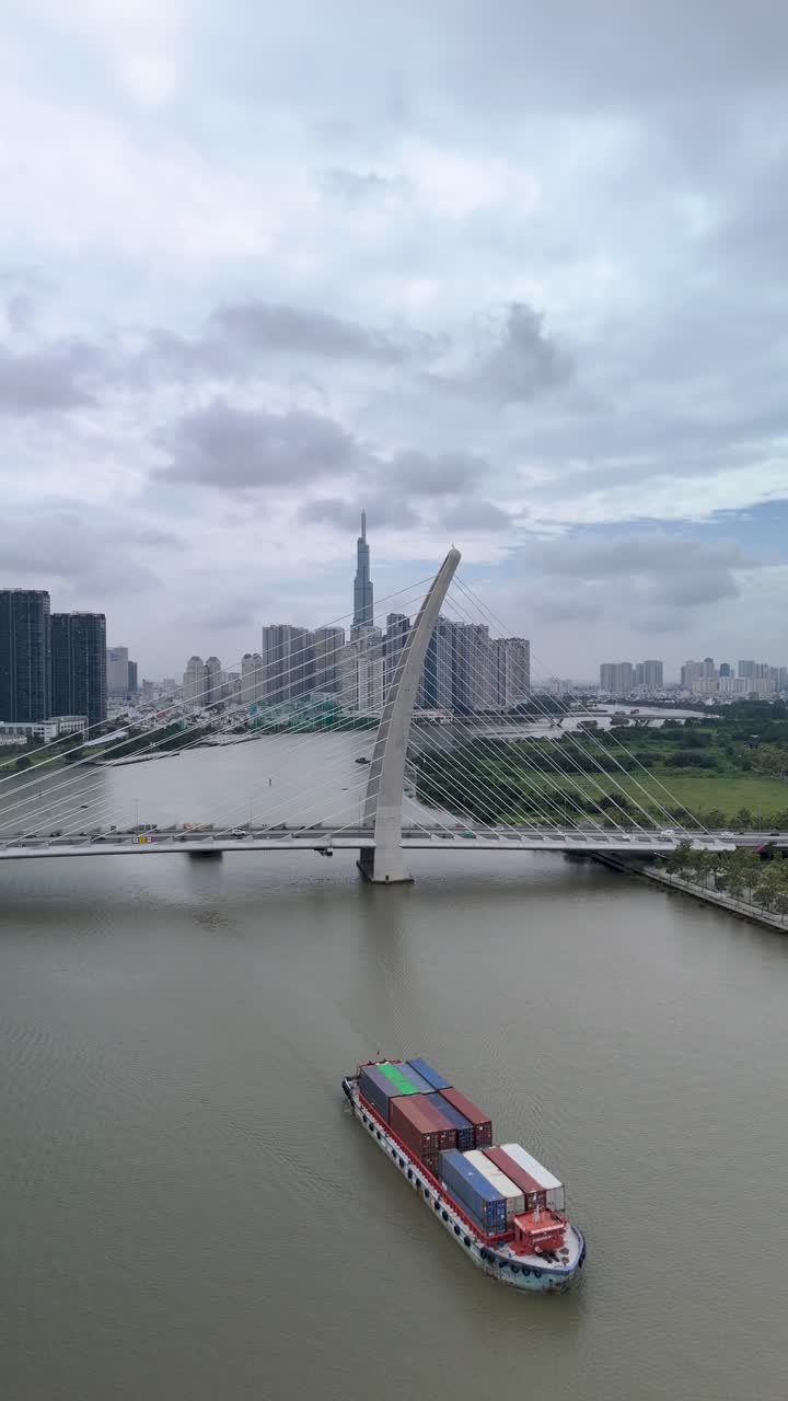 호치민 시의 사이곤 강에 있는 컨테이너 보트, 수직 형식의 랜드마크 건물과 함께 바손 서스펜션 브릿지의 공중 전망