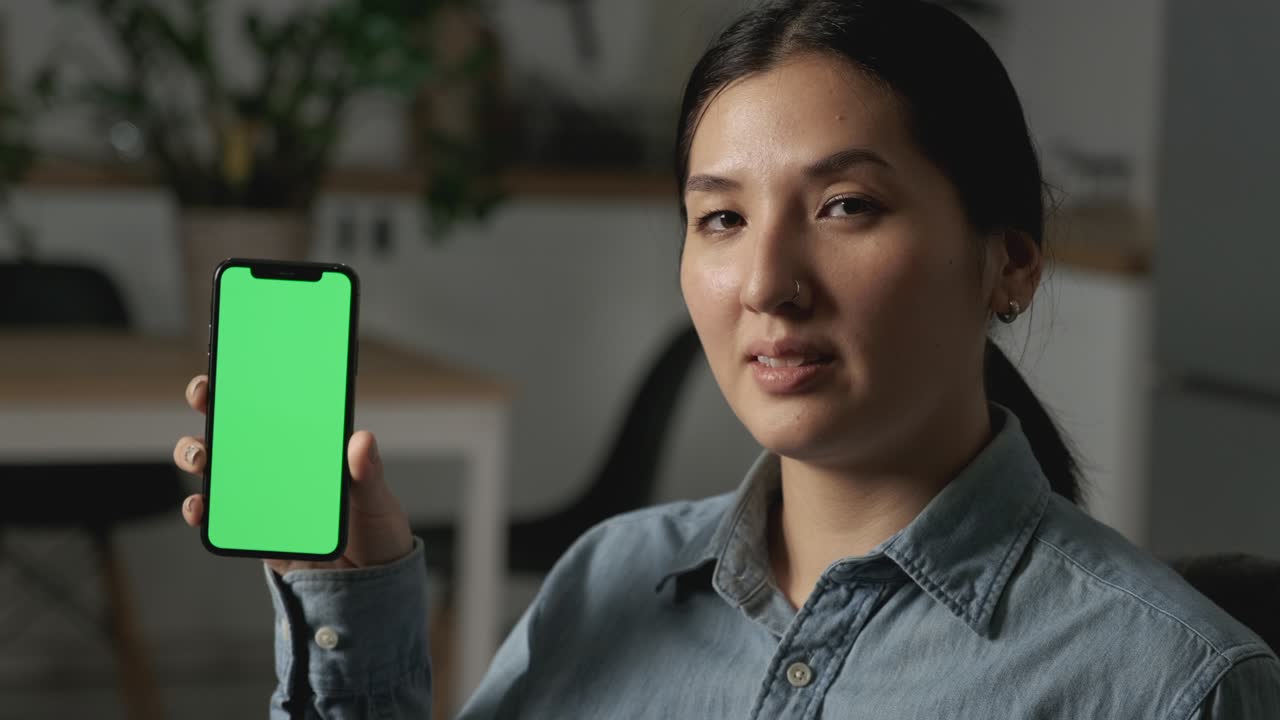 초록색 화면을 가진 전화를 보여주는 젊은 행복한 아름다운 다민족 여성. 카메라에 초록색 스크린을 보여주는 전화를 사용하는 젊은 예쁜 아시아 여성의 클로즈업 초상화