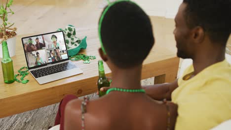 Smiling-diverse-group-of-friends-with-beer-wearing-clover-shape-items-on-video-call-on-laptop