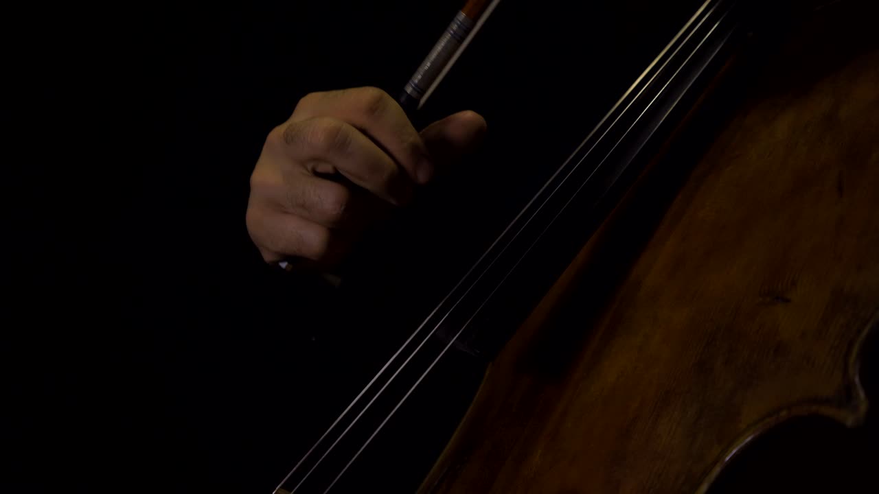 Close-up of cellist playing pizzicato notes with bow in hand.