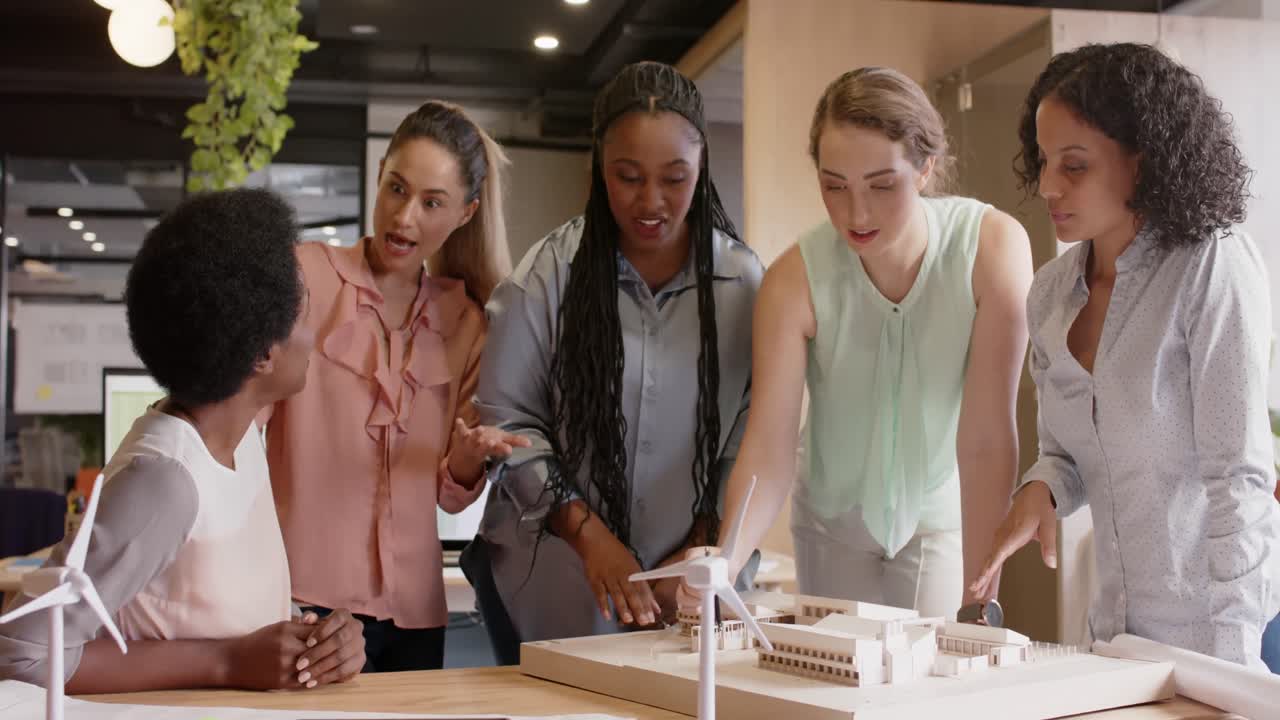 Diverse team of happy female architects discussing architectural model at work, in slow motion