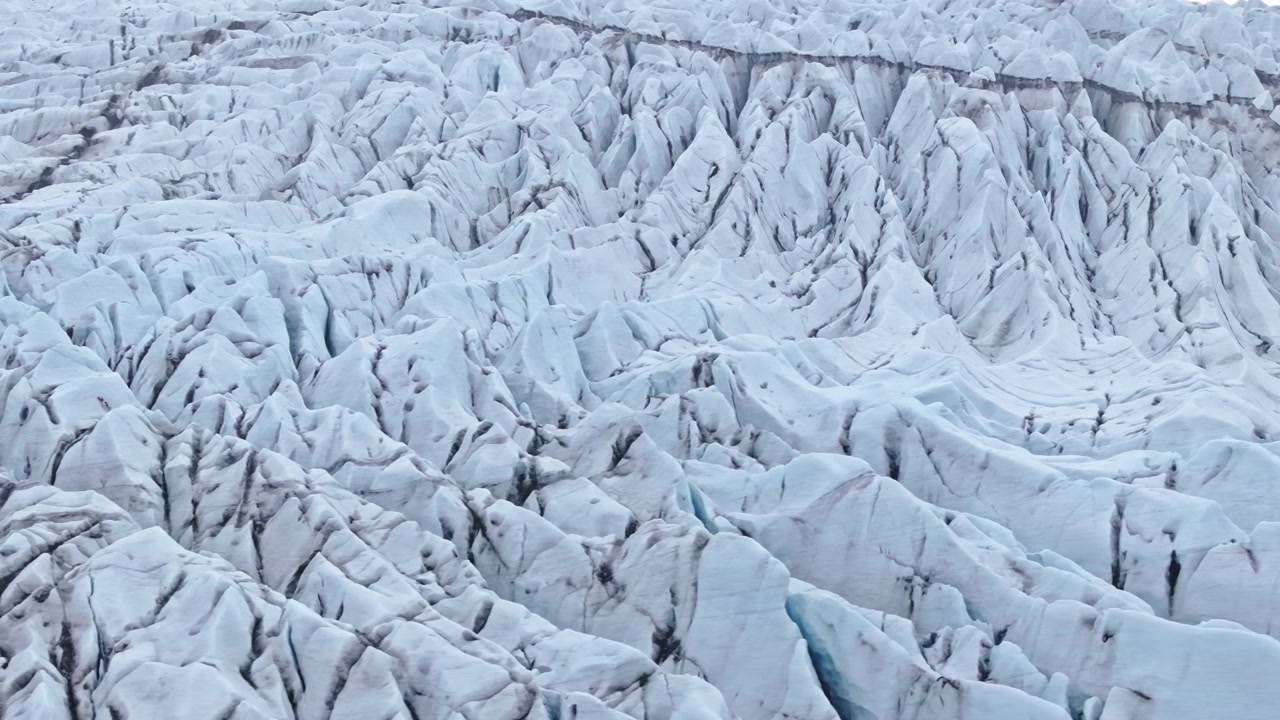 Veduta aerea astratta su crepacci di ghiacciaio testurizzati in Islanda. Intricato motivo di cime di ghiaccio frastagliate e profondi abissi. Campi di ghiaccio glaciale che si sciolgono rivelano strisce di cenere nera sporca da antiche eruzioni.
