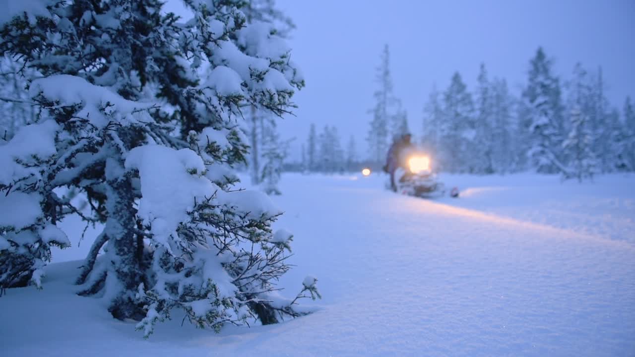 Snowmobiles speeding in a snowy woondland landscape, at dusk, in Lapland, Finland