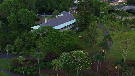 Aerial-view-drone-fly-around-colonial-georgian-style-Newstead-house-heritage-museum-at-the-bank-of-breakfast-creek-surrounded-by-green-trees-and-grassy-lawn,-Brisbane-inner-city-suburb