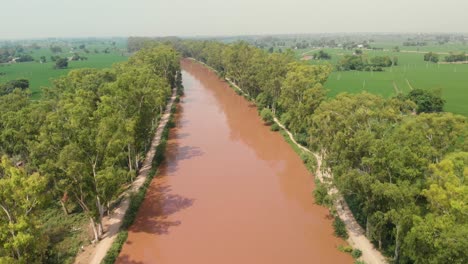 Una-Vista-Aérea-Del-Río-Fangoso-Que-Fluye-En-Medio-De-Los-árboles-Cerca-Del-área-Agrícola-En-La-Provincia-De-Punjab