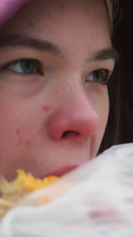primer plano de una joven con chaqueta de invierno disfrutando de comer maíz en la calle, sonriendo mientras come, chaqueta con capucha, clima frío, al aire libre, fondo borroso con nieve y árboles