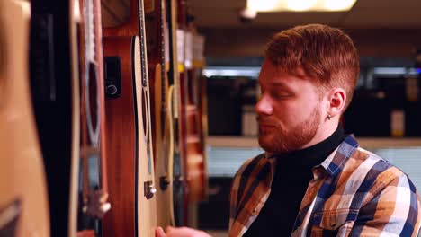 redhair ginger man is choosing quality acoustic guitar in guitar shop