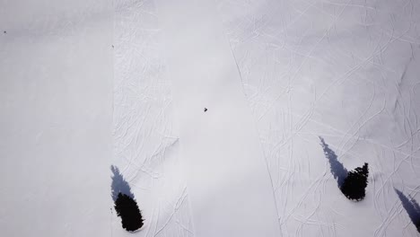 Skiers-skiing-downhill-the-ski-slope-during-winter-day-in-the-high-mountains,-aerial-view