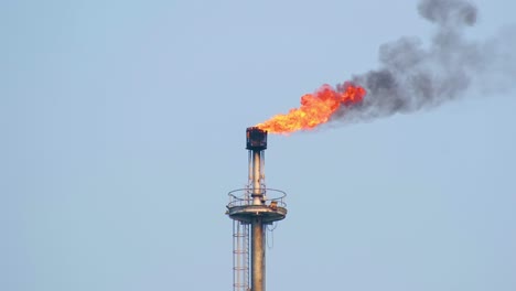 flames erupt out of an industrial chimney blowing smoke with the wind