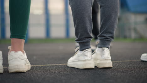 close-up of legs of three athletes in joggers and sneakers walking on court, with blurred background showing another athlete leg also in joggers and sneakers