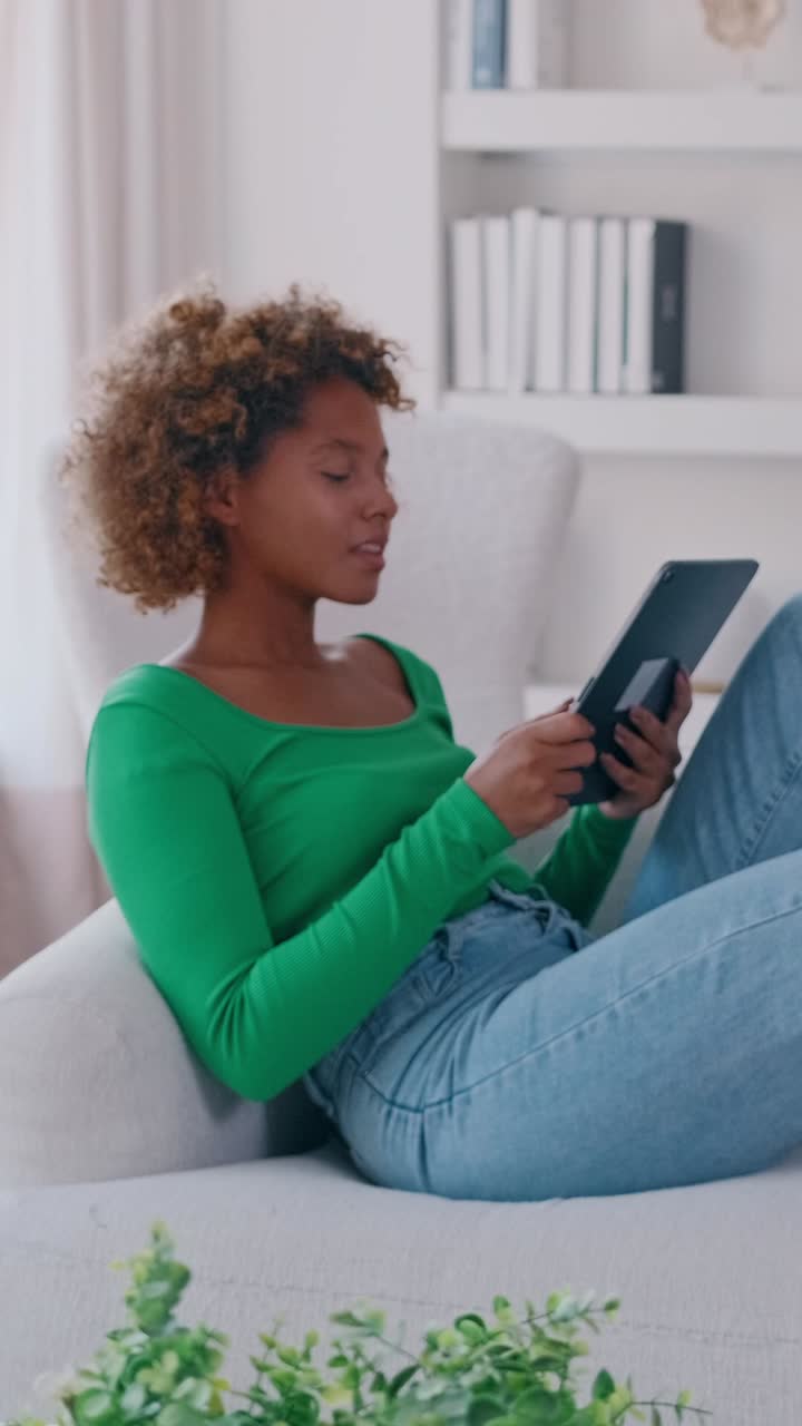 Young woman relaxing on a sofa at home reading a digital tablet and smiling