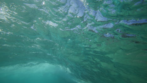 surfista montando en una ola en aguas cristalinas en la bahía de byron, australia, disparado desde debajo del agua en cámara lenta.