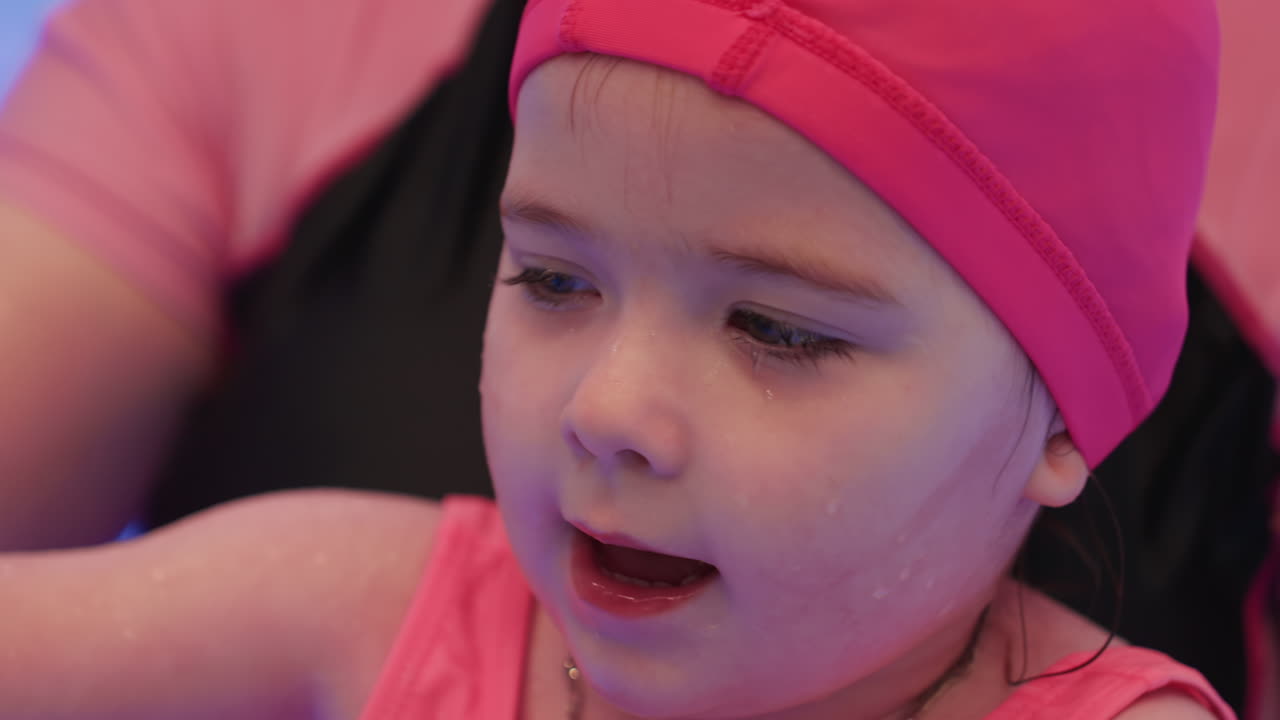 Close view of toddler resting on water with straight set lashes visible, face calm and relaxed, water gently supporting head as child floats peacefully and pacifically in pool environment
