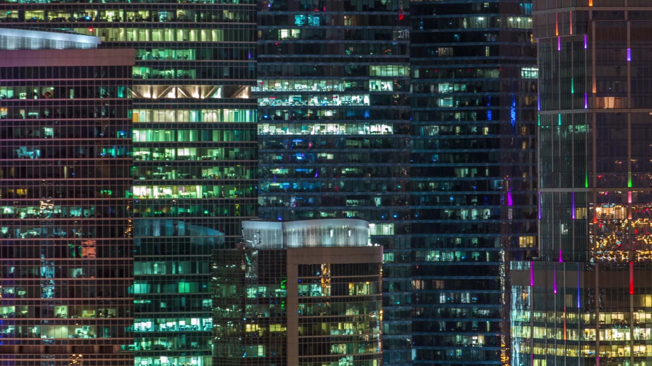 Modern office building with glowing windows at night timelapse. Moscow city. Close up view from rooftop. Pan right