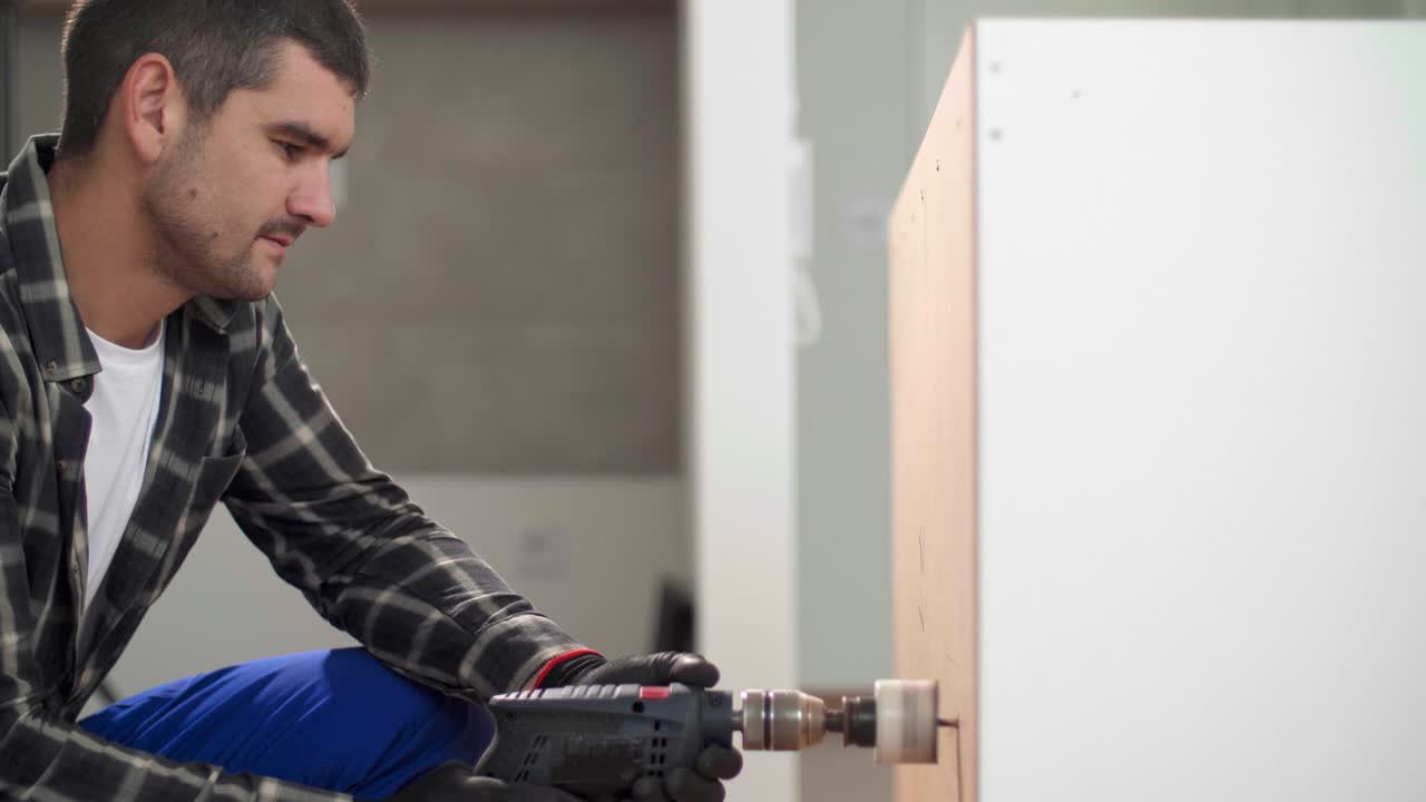 A carpenter with a circular drill drilling holes in the kitchen shelves.
