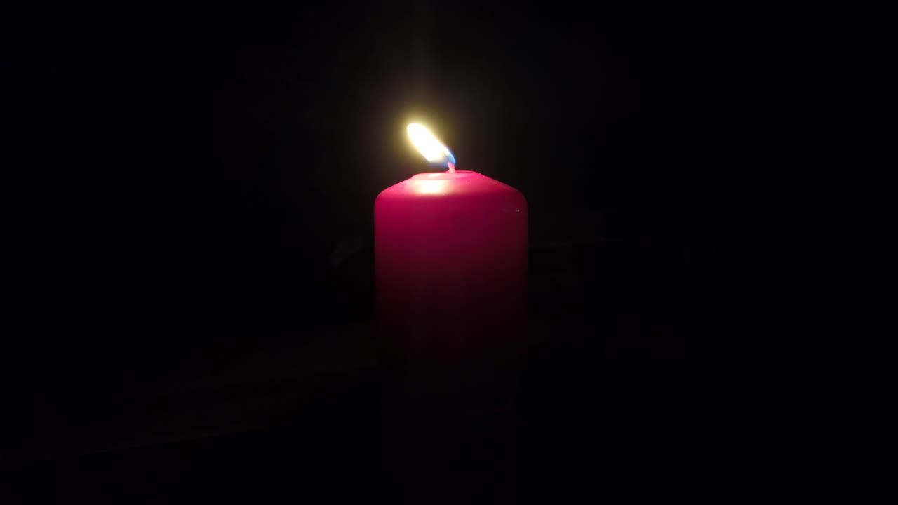 Primo piano di una candela rosa che brucia su uno sfondo nero