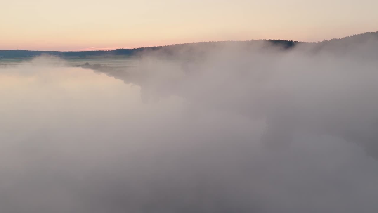 Drone over lake shrouded in mist, fog obscures trees on the shore, creating a mysterious atmosphere, pullback