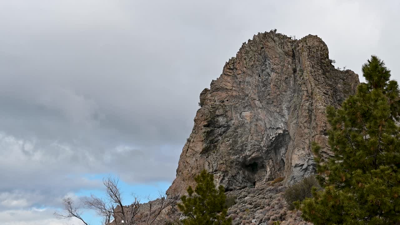 Aerial drone view of a rugged rocky cliff rising sharply above trees with dramatic sky in the background