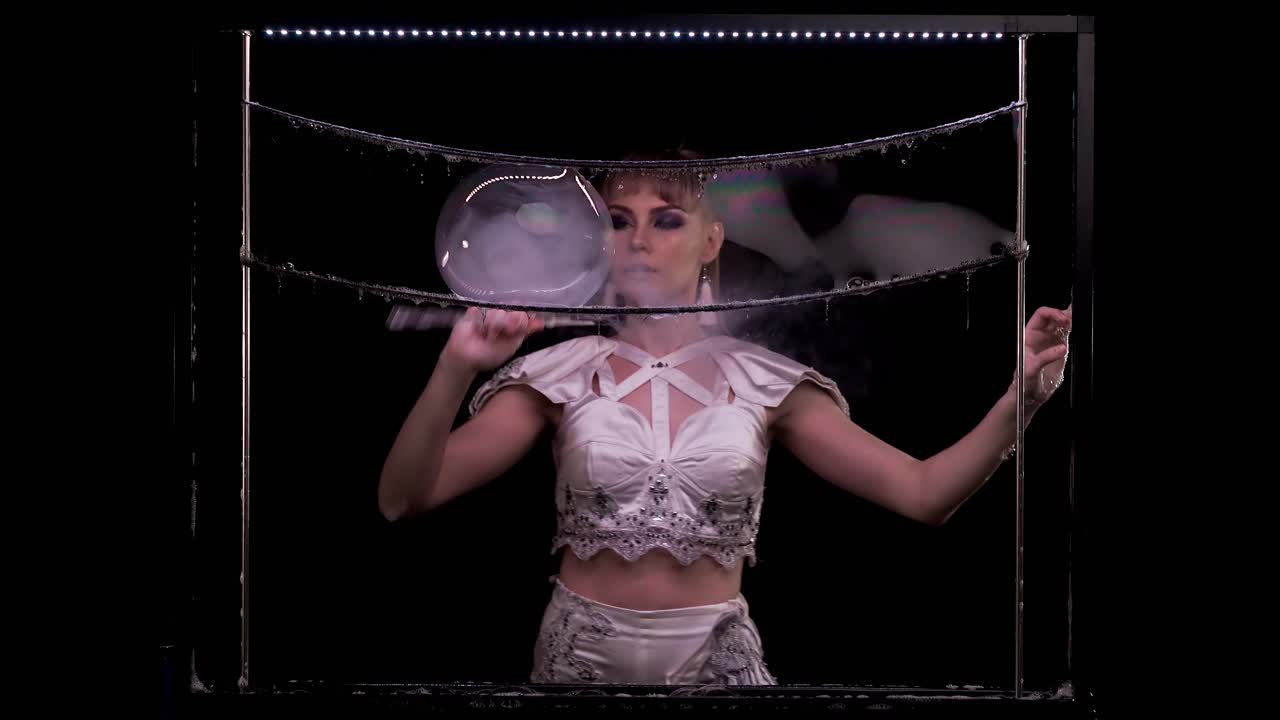 예쁜 여자는 비누 거품으로 묘기를 부리고 파이프로 거품을 부수며 색상 하이라이트로 시선을 따라갑니다