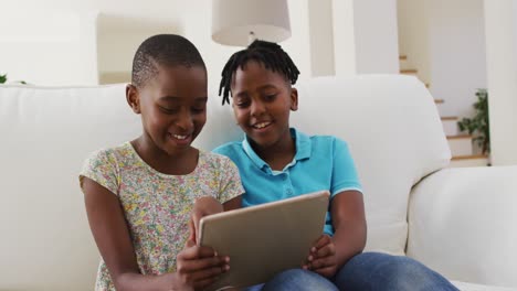 Afroamerikanische-Jungen-Und-Mädchen-Nutzen-Ein-Digitales-Tablet,-Während-Sie-Zu-Hause-Auf-Der-Couch-Sitzen