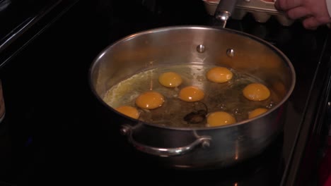 close up shot of a young adult male cracking an egg into a large pan full of eggs