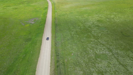 aerial view of car traveling down dirt road with stunning green grass surrounding it