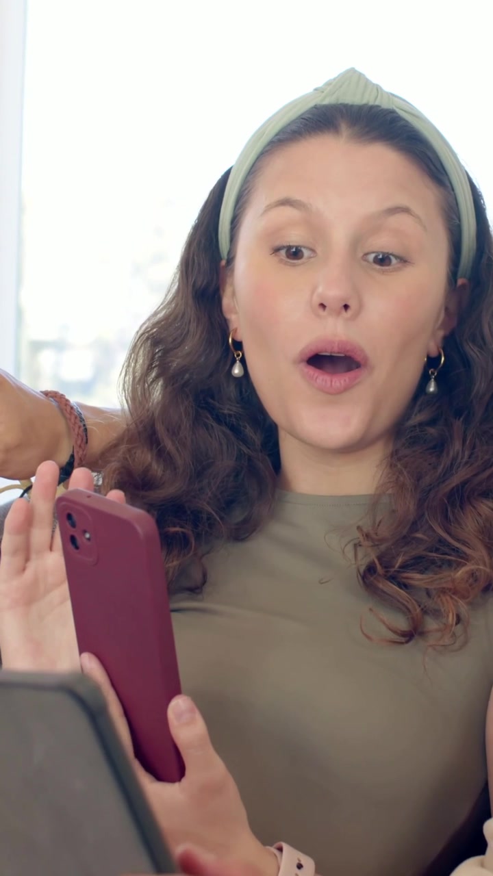 Video verticale: Braccio che indica esortando una donna che tocca un telefono bordeaux sul divano e controlla un tablet per visualizzare.
