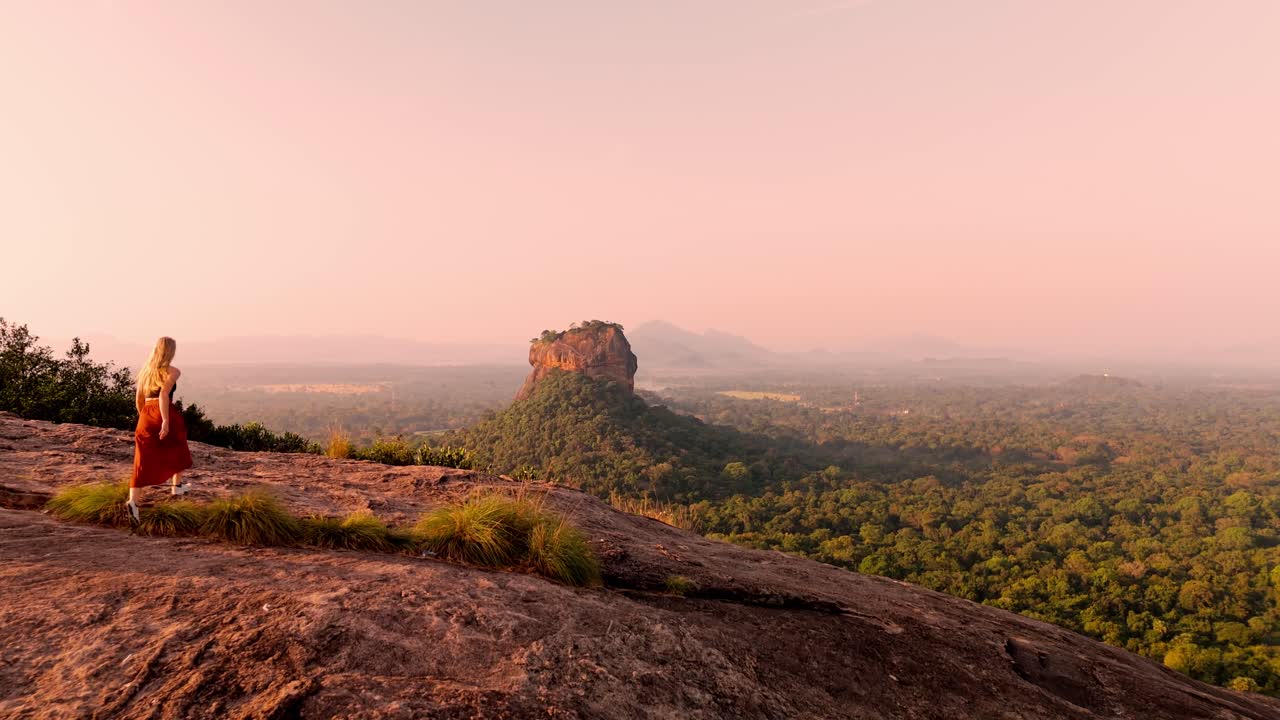 A young woman runs across the summit of Pidurangala Rock to catch the magical sunrise over Sigiriya Rock.