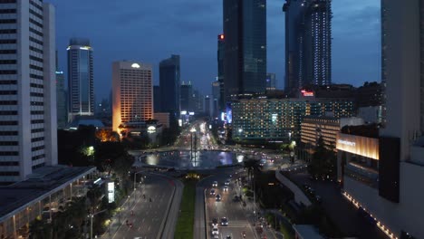 aerial dolly retreating shot of cars driving around the selamat datang monument in the city center of jakarta at night