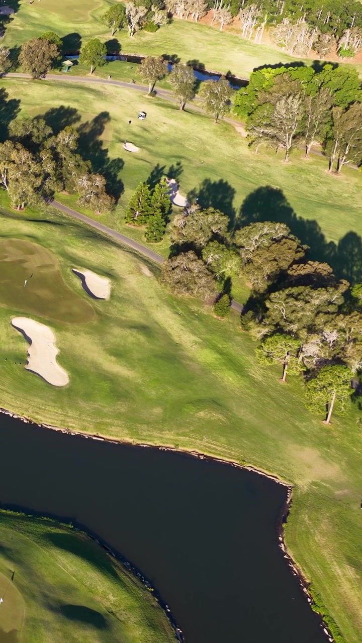 Tomada aérea de drone revela uma paisagem cênica de campo de golfe com fairways, lagos e bunkers de areia.