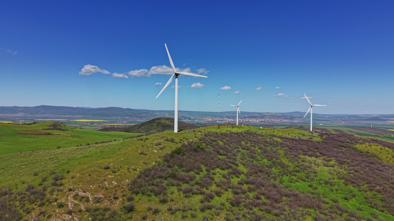 Aerogeradores erguem-se em uma colina verde sob um céu azul claro.