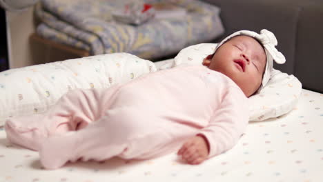 cute baby in pink outfit napping on a bed with a white bow on her head. a calm and peaceful moment captured with softness and warmth