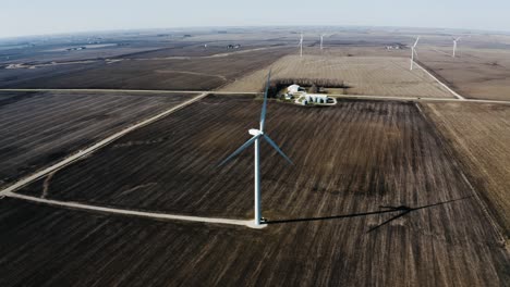 drone pulling away from a rural wind turbine spinning amidst the fields of brown