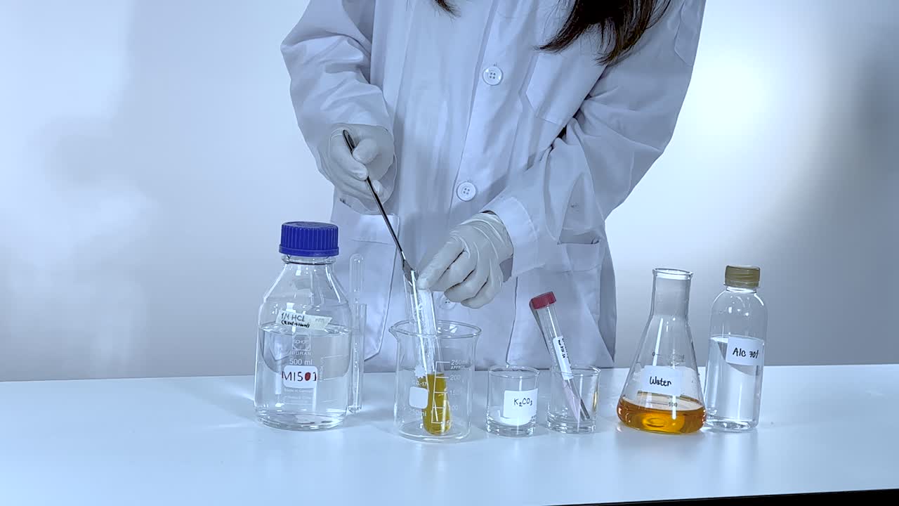 A scientist in a lab coat performs a chemical experiment with potassium carbonate, using various glassware under bright lighting
