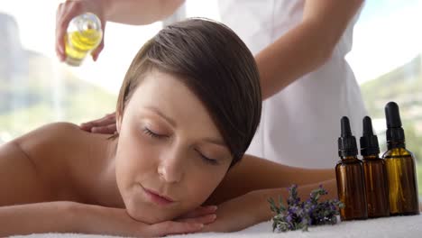 masseur pouring massage oil on the back of her patient