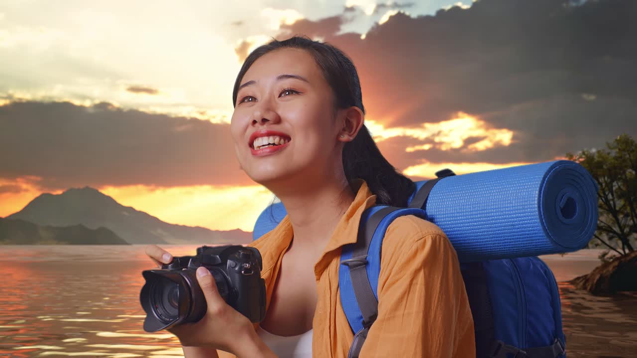 vista lateral de cerca de una excursionista asiática con mochila de montañismo sonriendo y sosteniendo una cámara en sus manos luego mirando a su alrededor mientras está de pie en un lago durante la hora del atardecer