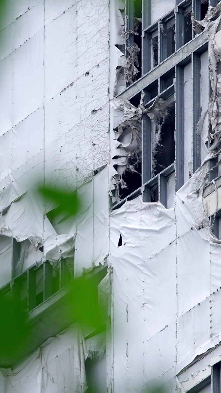 Facciata di edificio danneggiata con materiale bianco scrostato e struttura metallica a vista